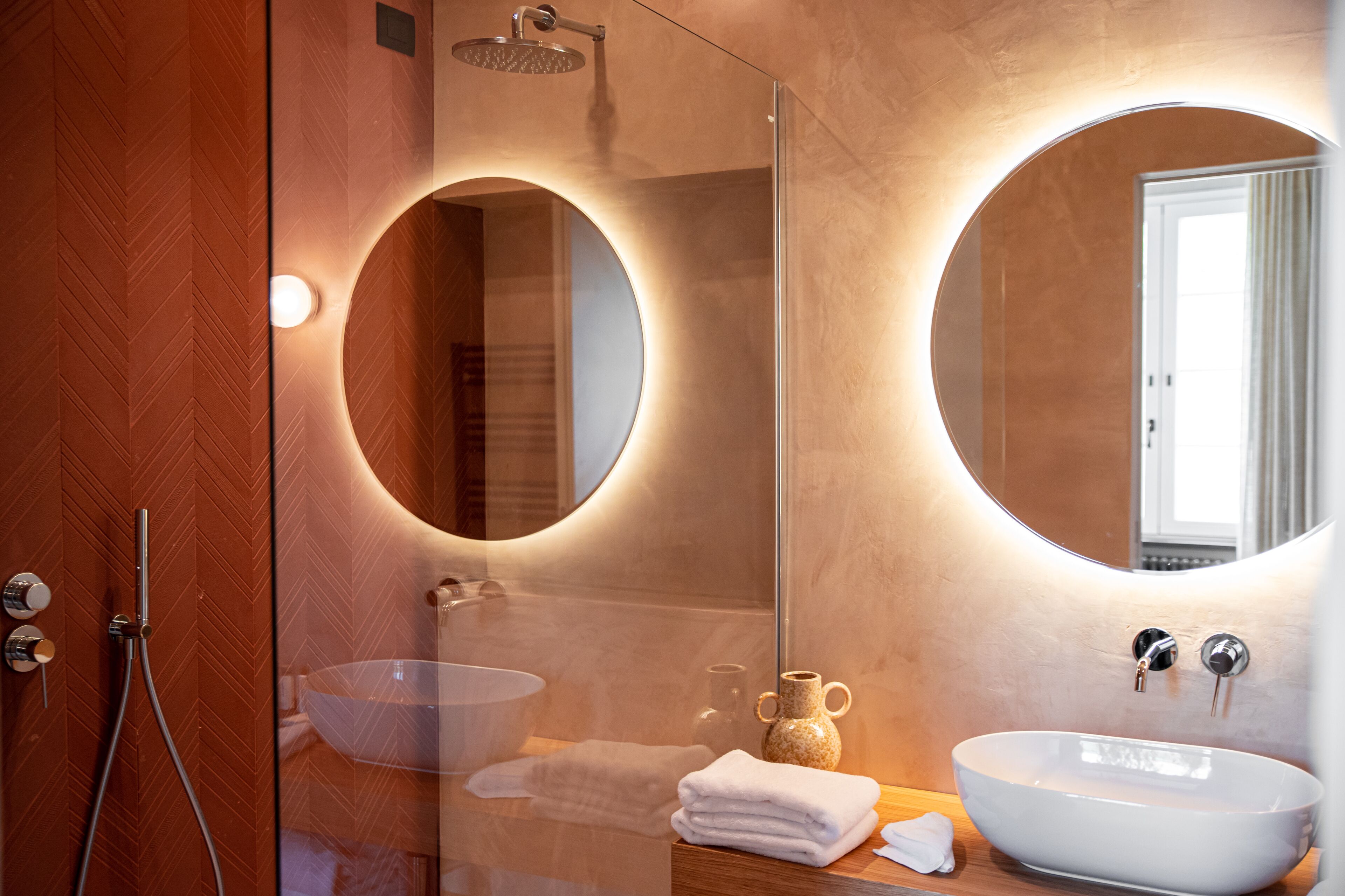 A modern bathroom with a glass-enclosed shower, a round mirror, and a white sink.