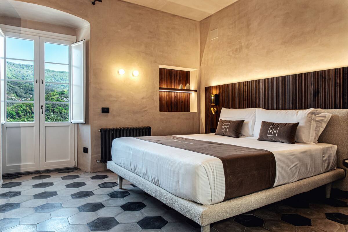 A bedroom with a large bed, a view of greenery through a door, and a wooden panel wall.