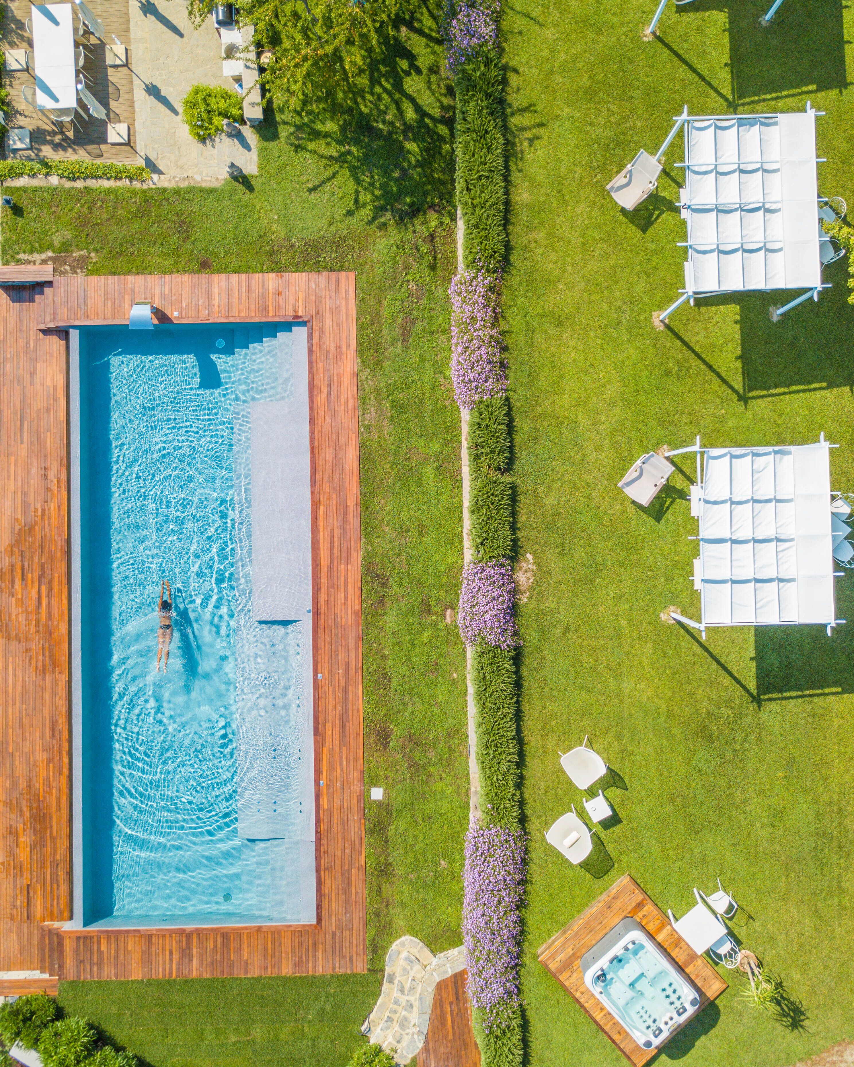An aerial view of a swimming pool area with a wooden deck, a hot tub, and outdoor seating.