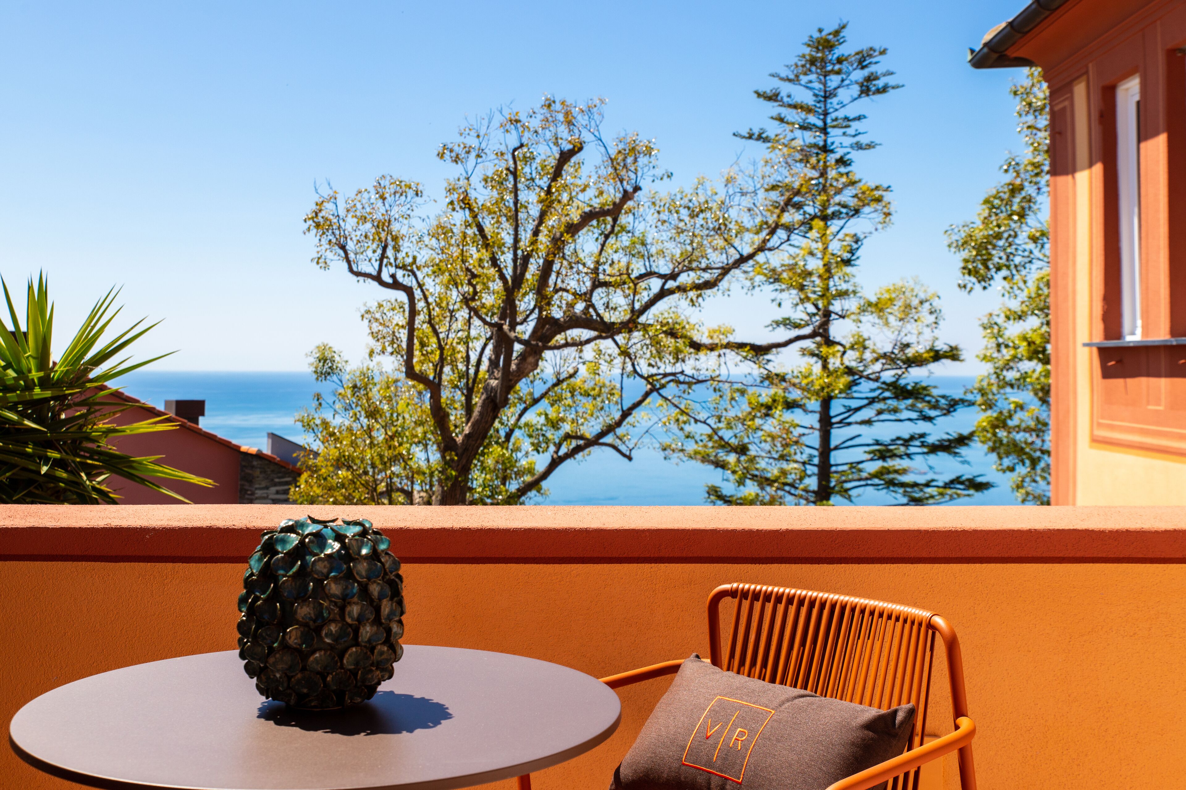 A round table with a pineapple centerpiece, a wicker chair with a cushion, and a view of the sea and trees.