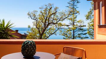 A round table with a pineapple centerpiece, a wicker chair with a cushion, and a view of the sea and trees.