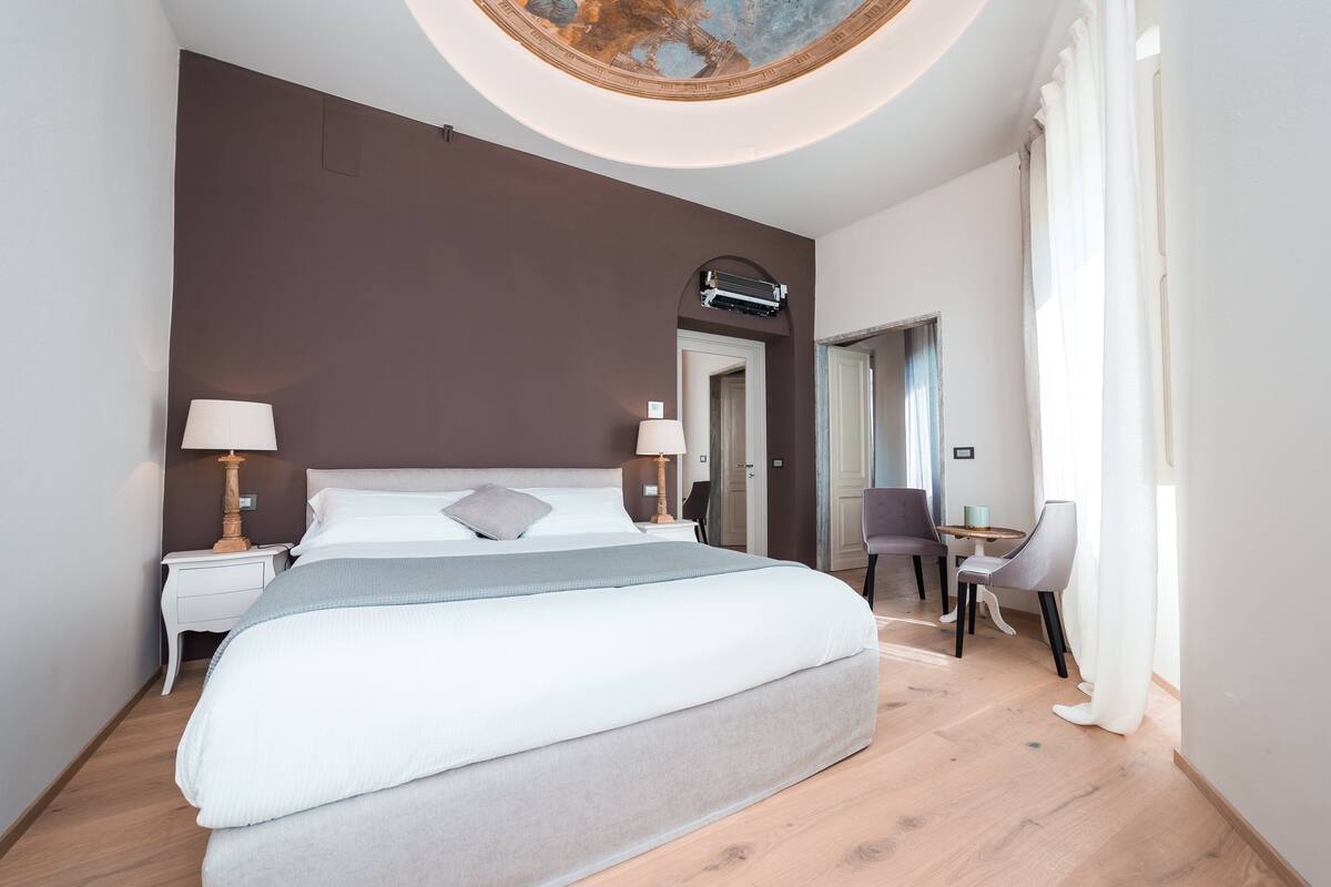 A modern hotel room with a large bed, bedside tables, a desk, and a chair.