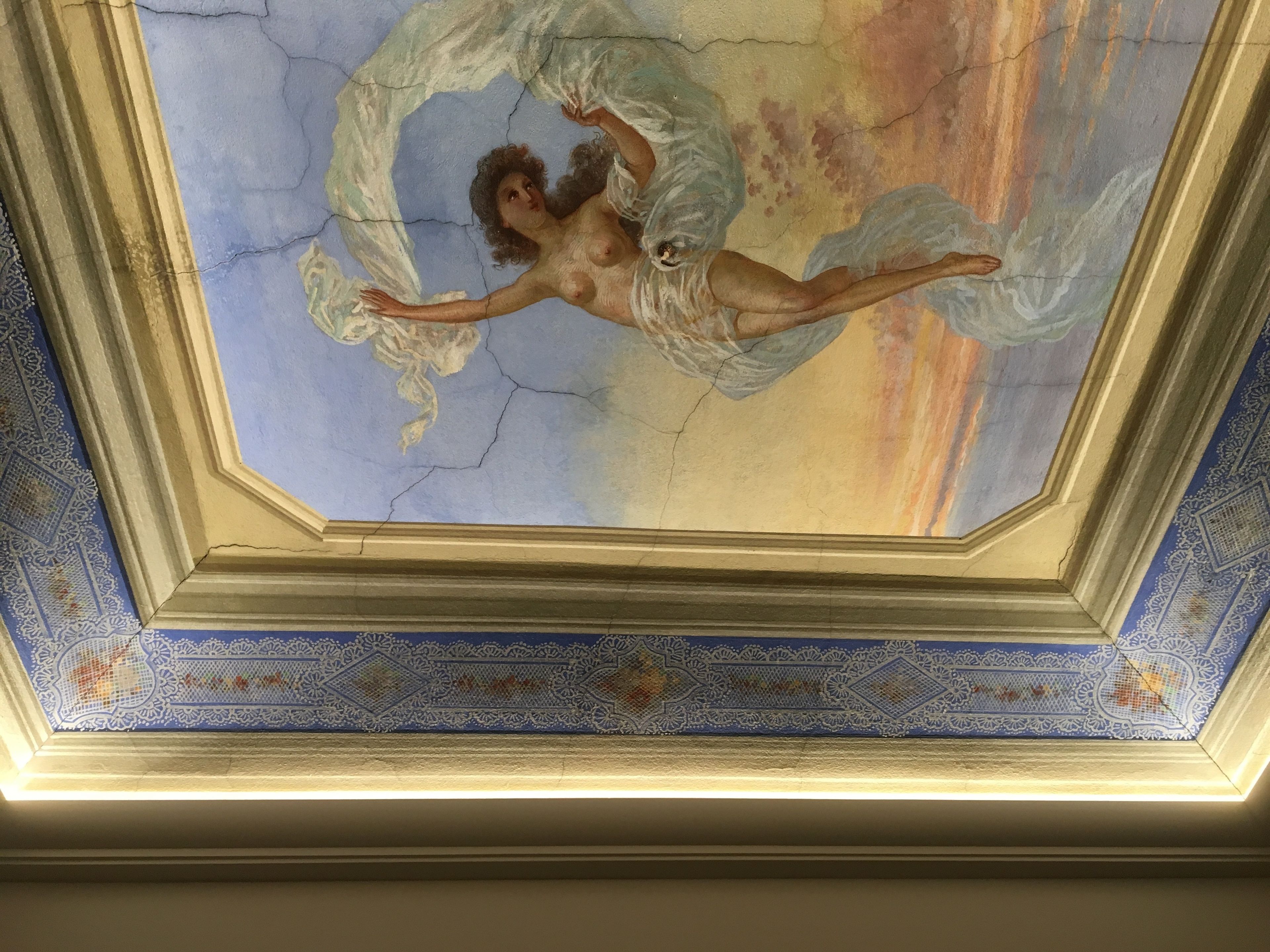 A ceiling with a fresco of a winged figure and cracked plaster.