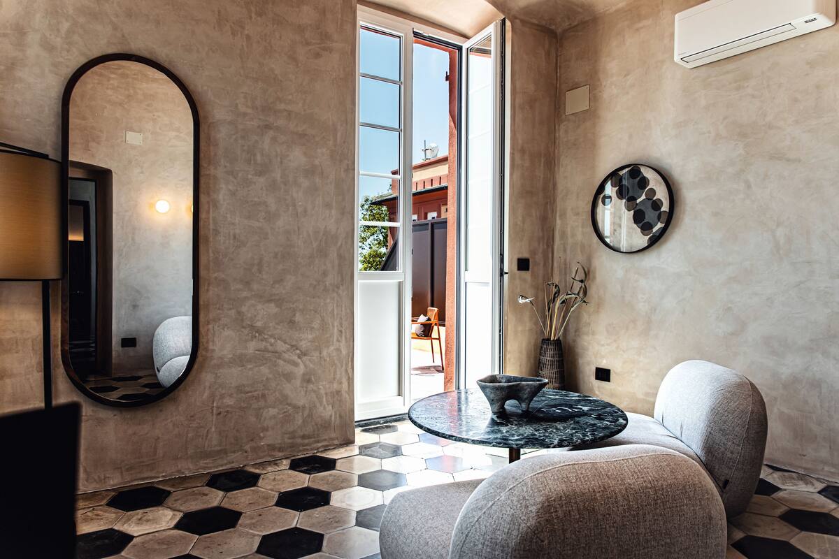 A modern interior with a round table, a sofa, a large mirror, and a view through a glass door.