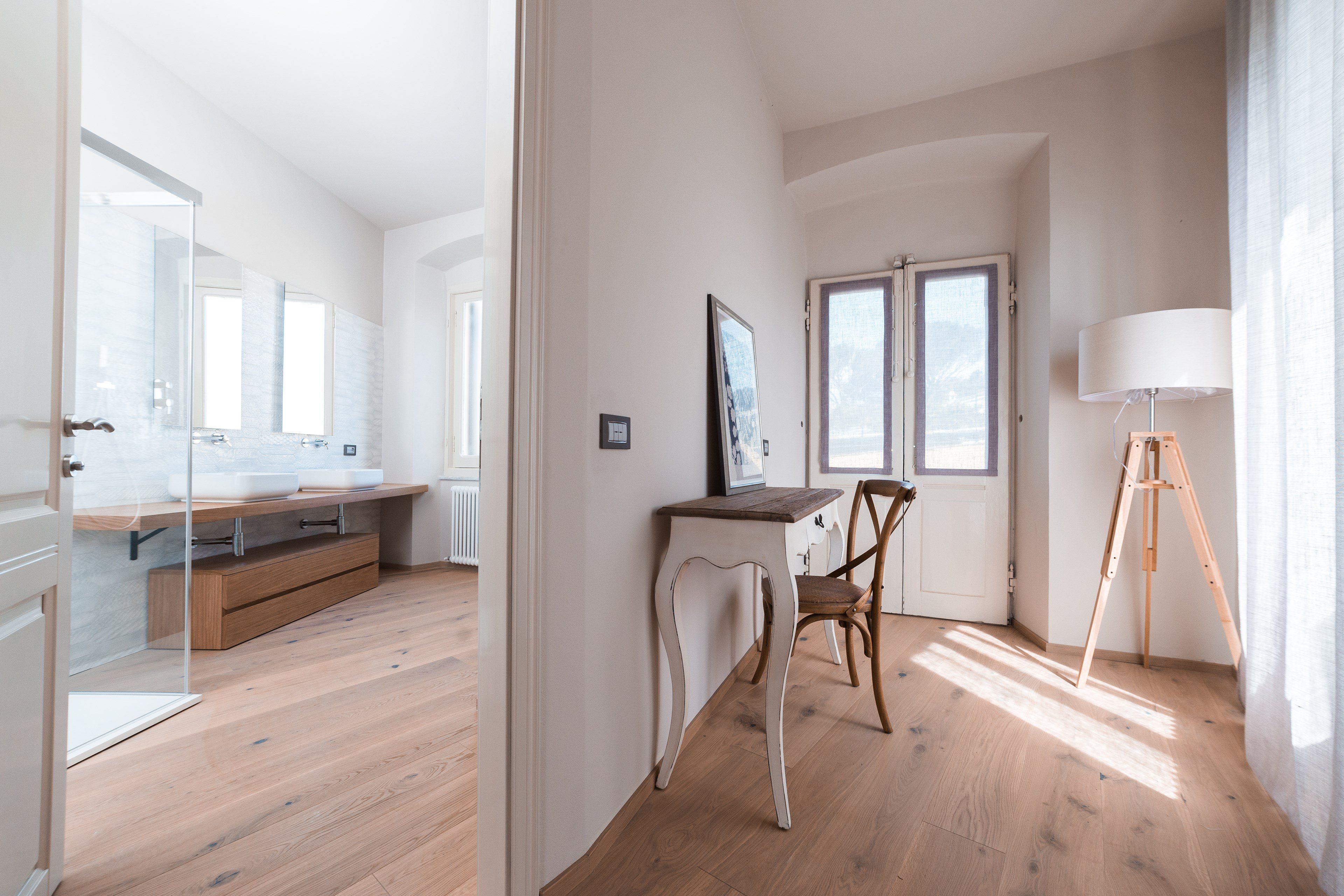 Una camera moderna con pavimento in legno, una scrivania con sedia, una lampada da terra e un'ampia finestra.