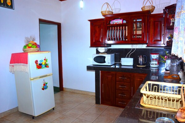 A compact kitchen with a refrigerator, microwave, and wooden cabinets. - Seasand Villa (Wadduwa)