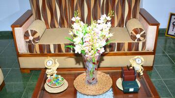 Um sofá de madeira com encosto estampado, um vaso com flores e duas figuras decorativas sobre uma mesa de madeira.