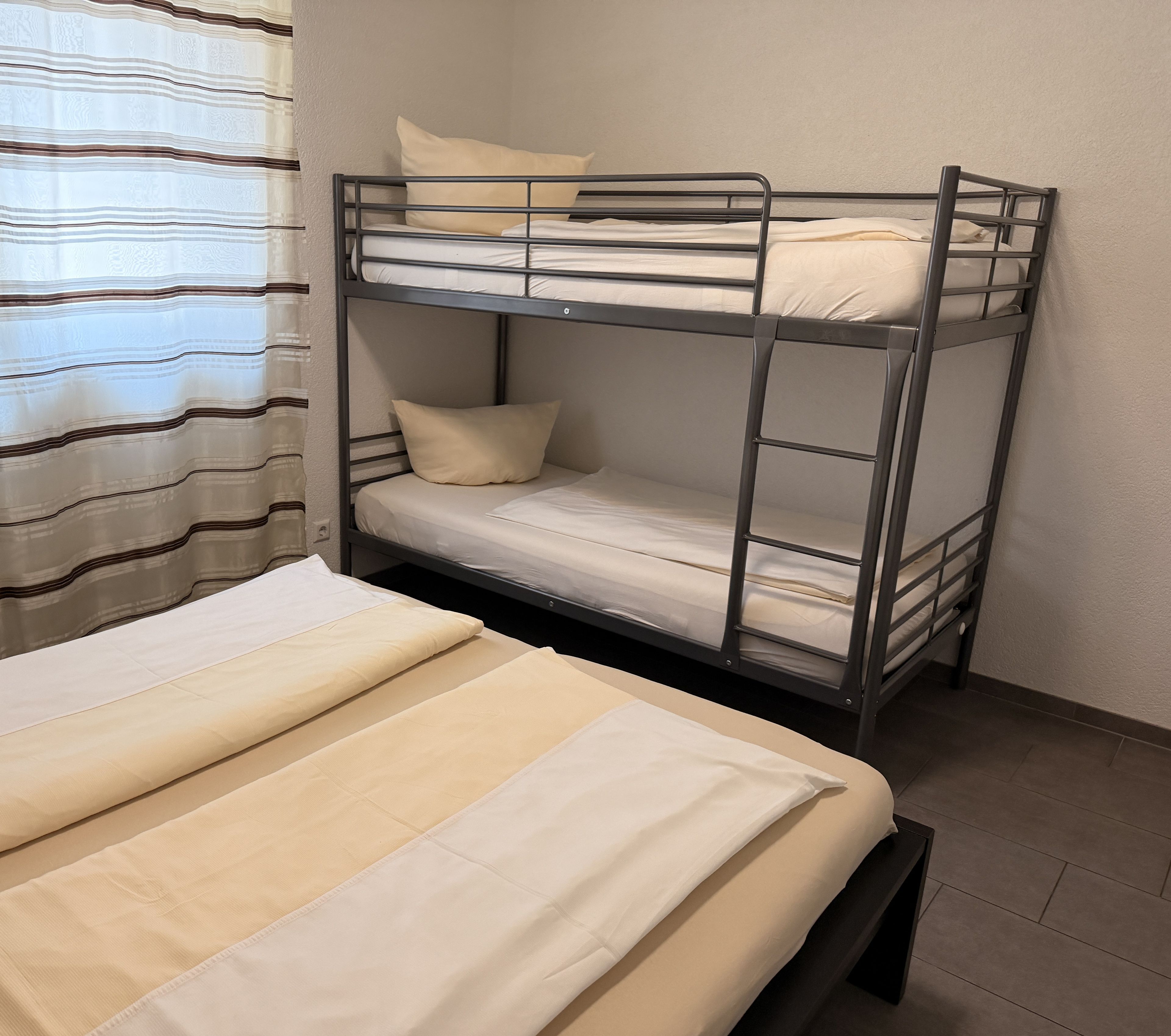 Ein Stockbett mit einer Unterliege und einem Einzelbett, beide mit weißer Bettwäsche.