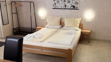 Ein ordentlich bezogenes Bett mit weißen Leinen und Handtüchern, zwei Nachttische, ein Holzstuhl und ein an der Wand befestigtes Kunstwerk.