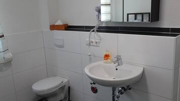 Un baño con inodoro blanco, lavamanos con espejo y suelo de baldosas negras.