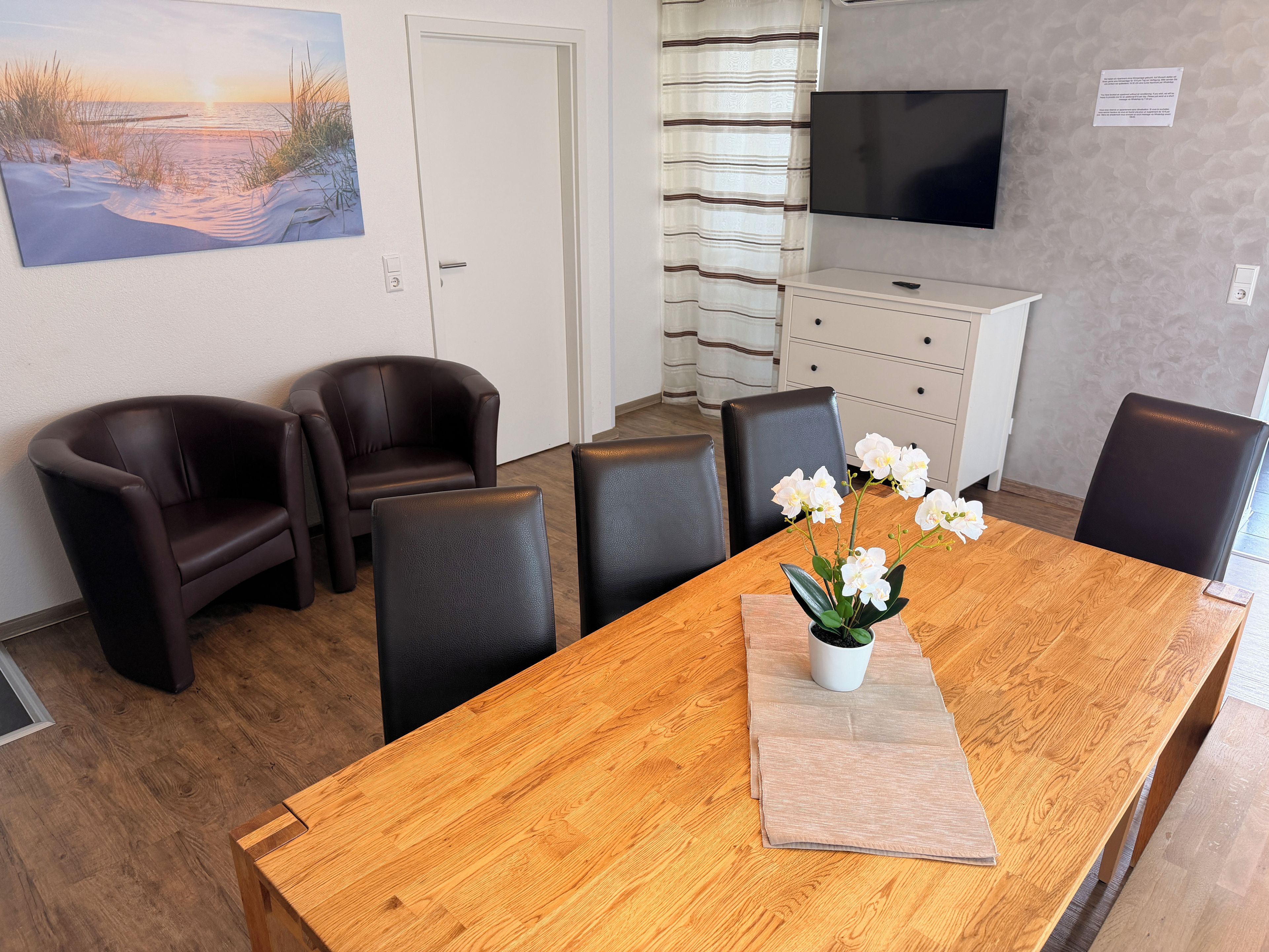 Un salón de conferencias con una mesa de madera, seis sillas, un televisor y un cuadro de una playa.