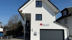 A two-story HILDA apartments building with a white facade, a garage, and a check-in box sign. - Hilda Apartments Rust (Rust)
