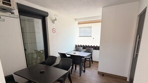 A compact living space with a dining area featuring a table and chairs, a sliding glass door, a ceiling fan, and a window with blinds. - Hilda Apartments Rust (Rust)