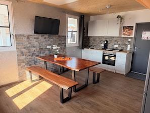 A modern kitchen with a wooden table, bench, stone backsplash, and a flat-screen TV. - Hilda Apartments Rust (Rust)