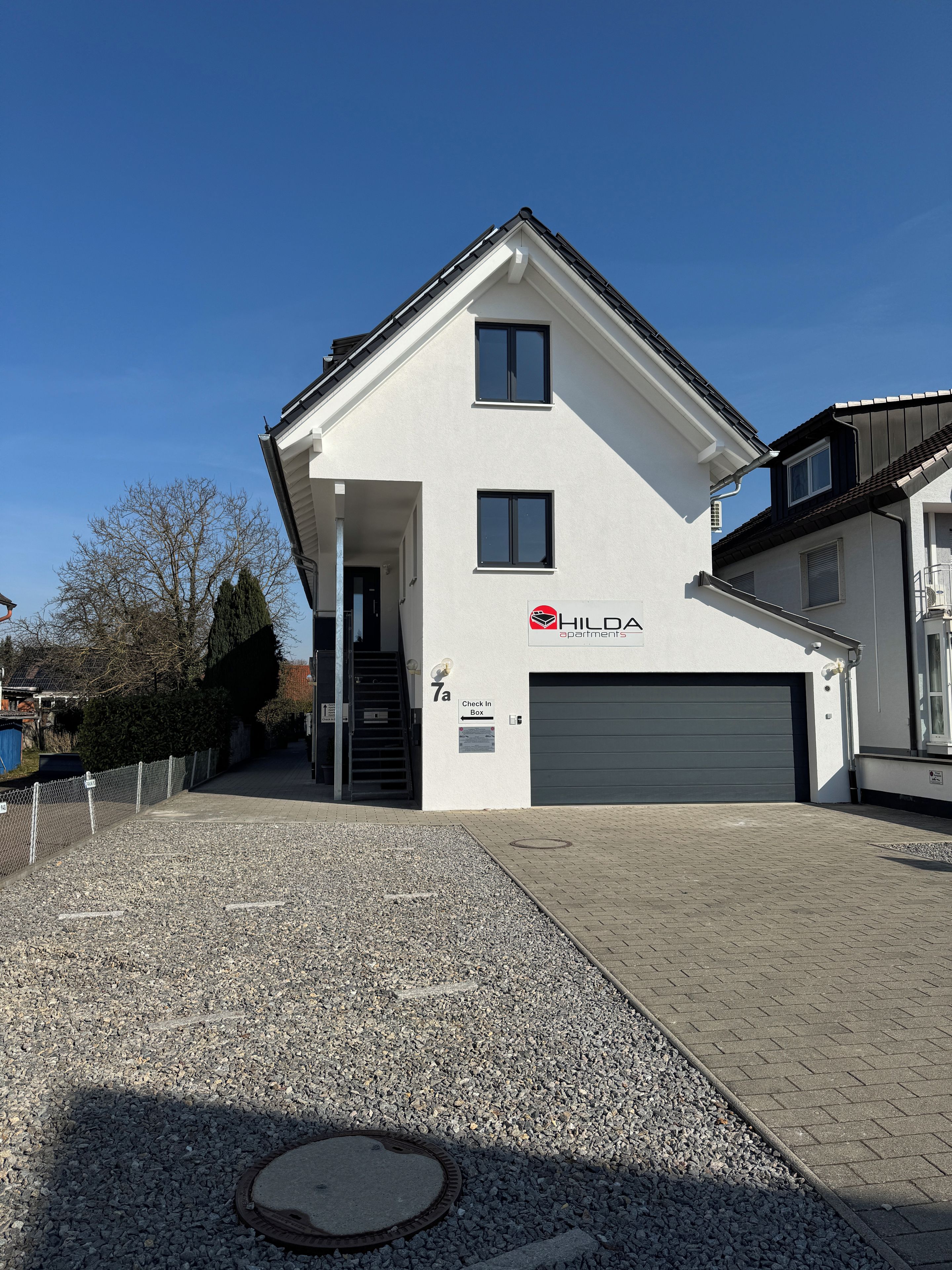 En toetages bygning med hvid facade, garageport og et skilt med teksten 'Check In Box'.