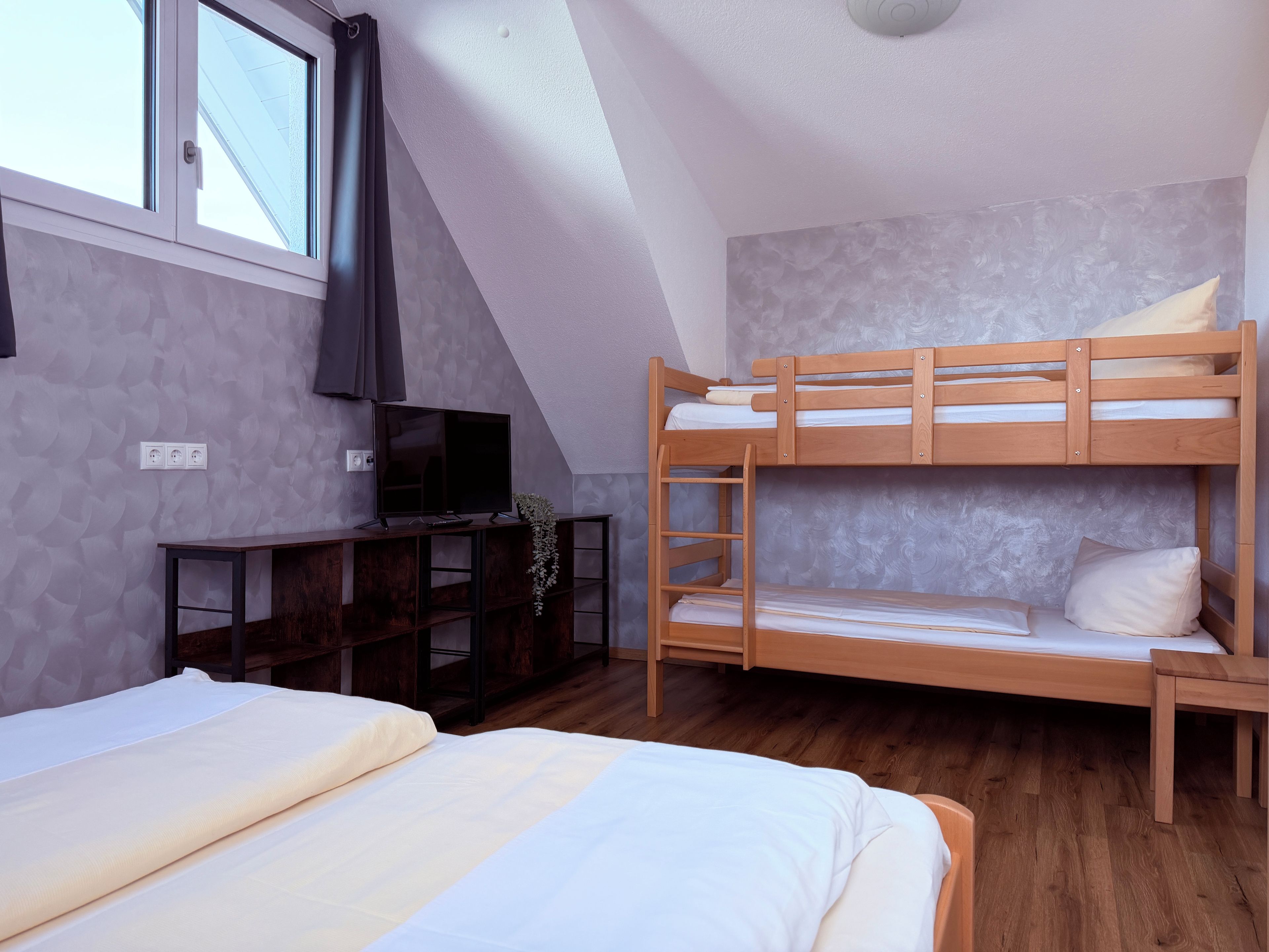 Una habitación con literas, un escritorio con televisor y una ventana con cortinas.