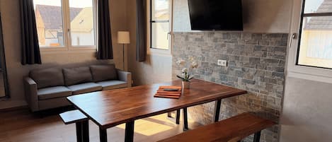 A modern living room with a sofa, a wooden dining table, and a stone accent wall.