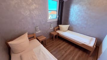 Une petite pièce avec deux lits, une fenêtre et un plancher en bois.