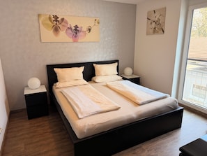 A neatly made bed with white linens, a black headboard, and two bedside tables with white lamps. - Hilda Apartments Rust (Rust)