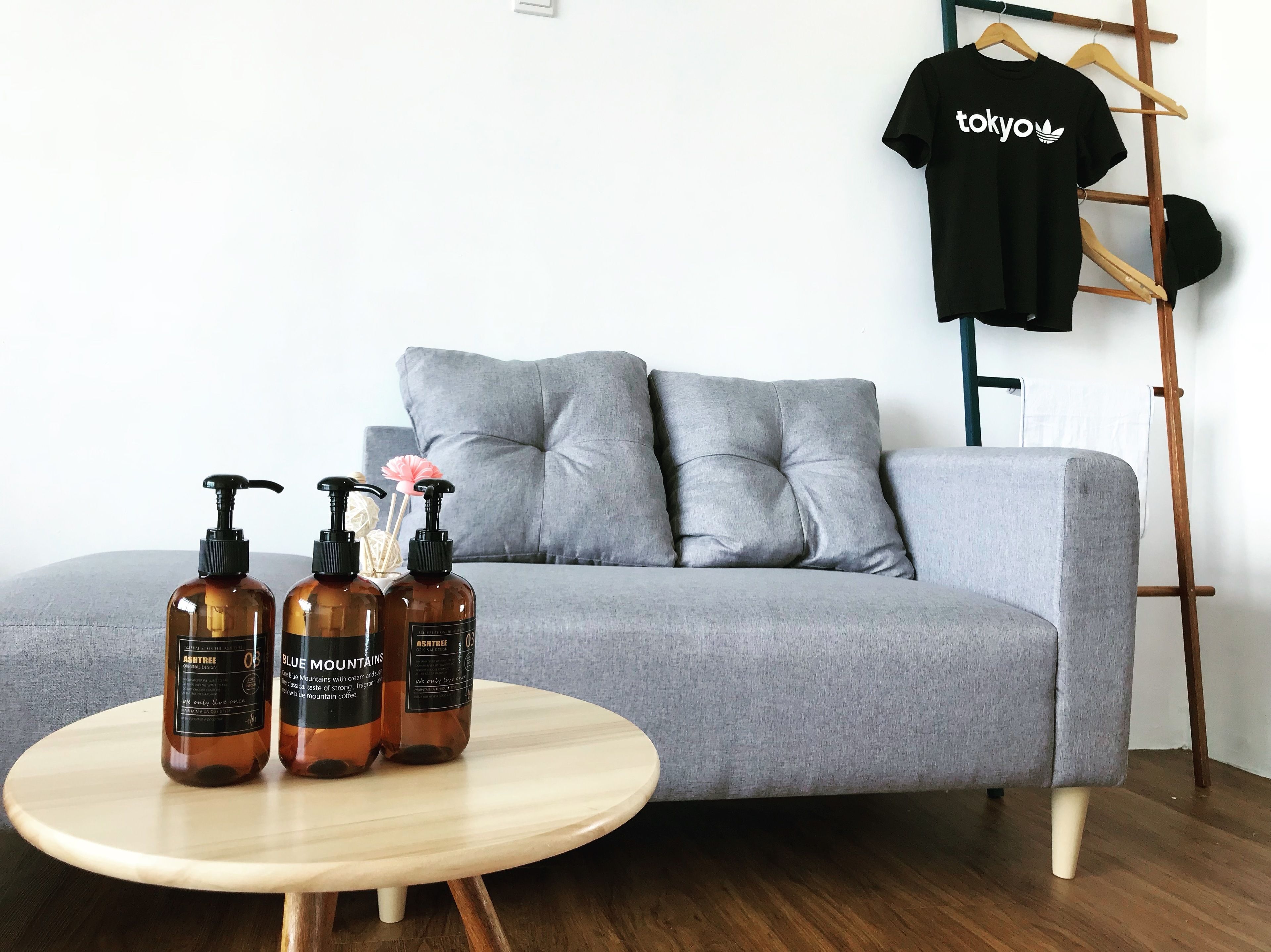 Ein graues Sofa, ein runder Holztisch mit drei braunen Flaschen und ein schwarzes T-Shirt mit dem Aufdruck 'tokyo'.