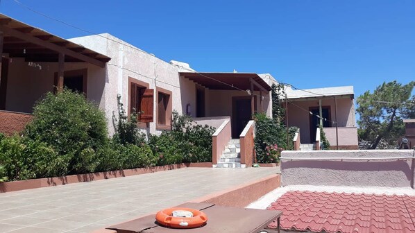 A building with a tiled patio, a lifebuoy, and a staircase leading to a covered area. - Ambeles Apartments (Sitia)