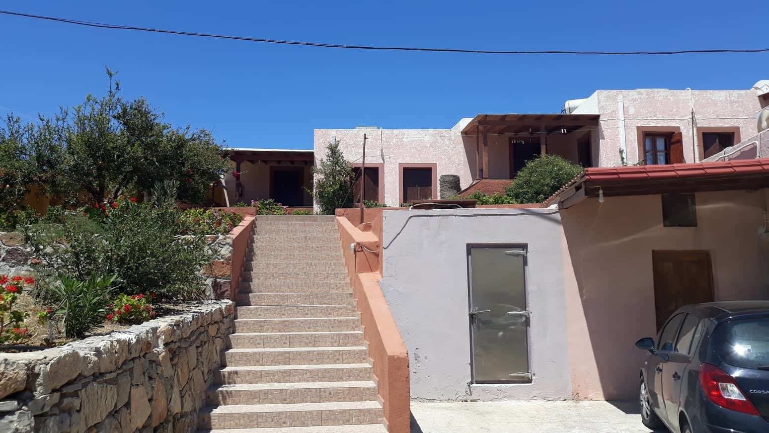 A residential building with a stone staircase leading to a door, a parked car, and a clear blue sky.