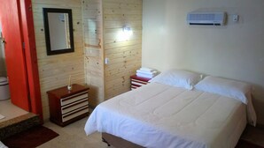 A bedroom with a bed, a wooden wardrobe, a mirror, and an air conditioning unit. - Pousada Casa João e Maria II (Gramado)