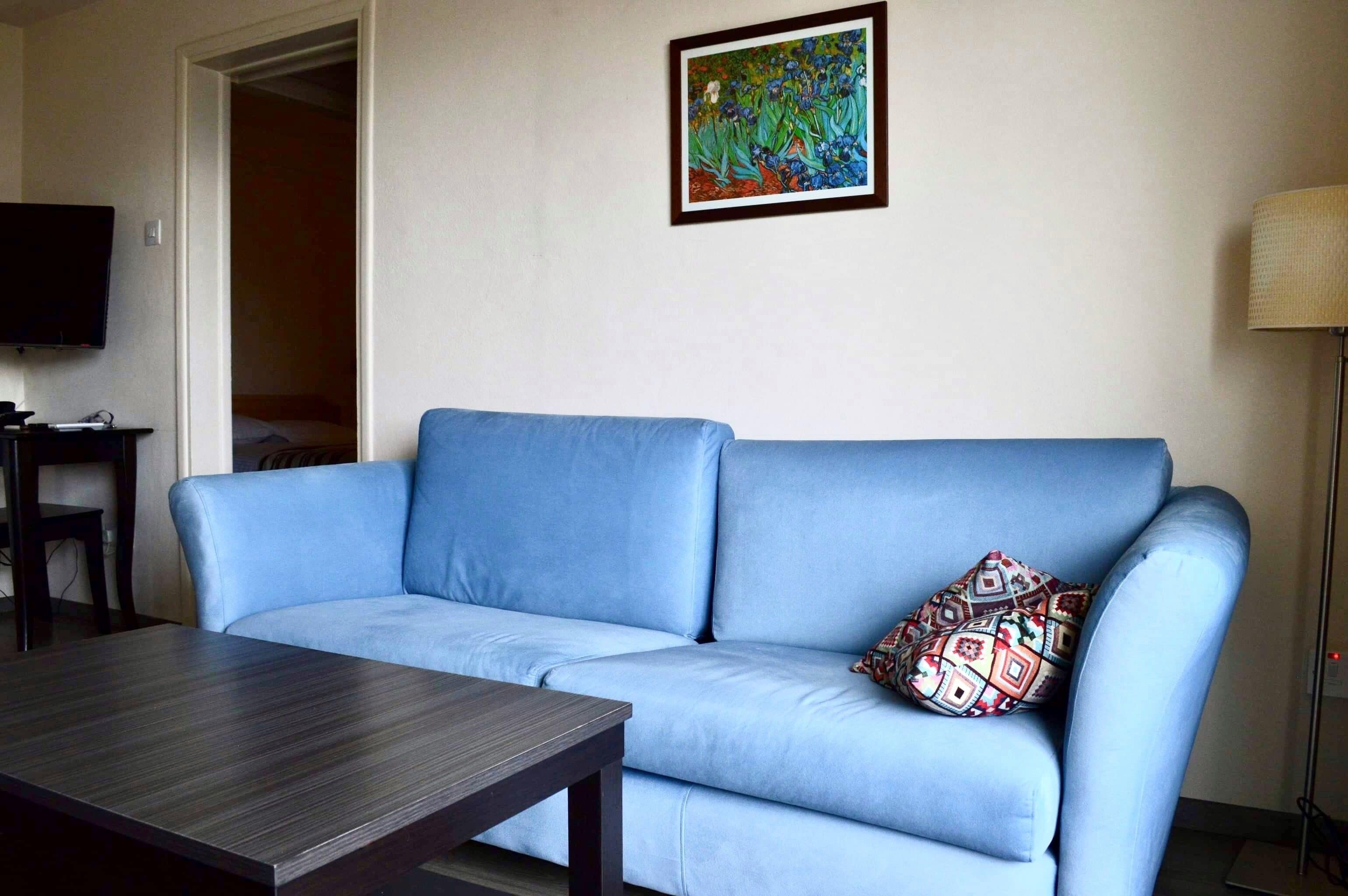 Una sala de estar con un sofá azul, una mesa de centro de madera, un televisor y un cuadro en la pared.