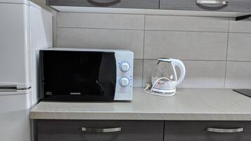 A kitchen with a microwave, kettle, and a white refrigerator.