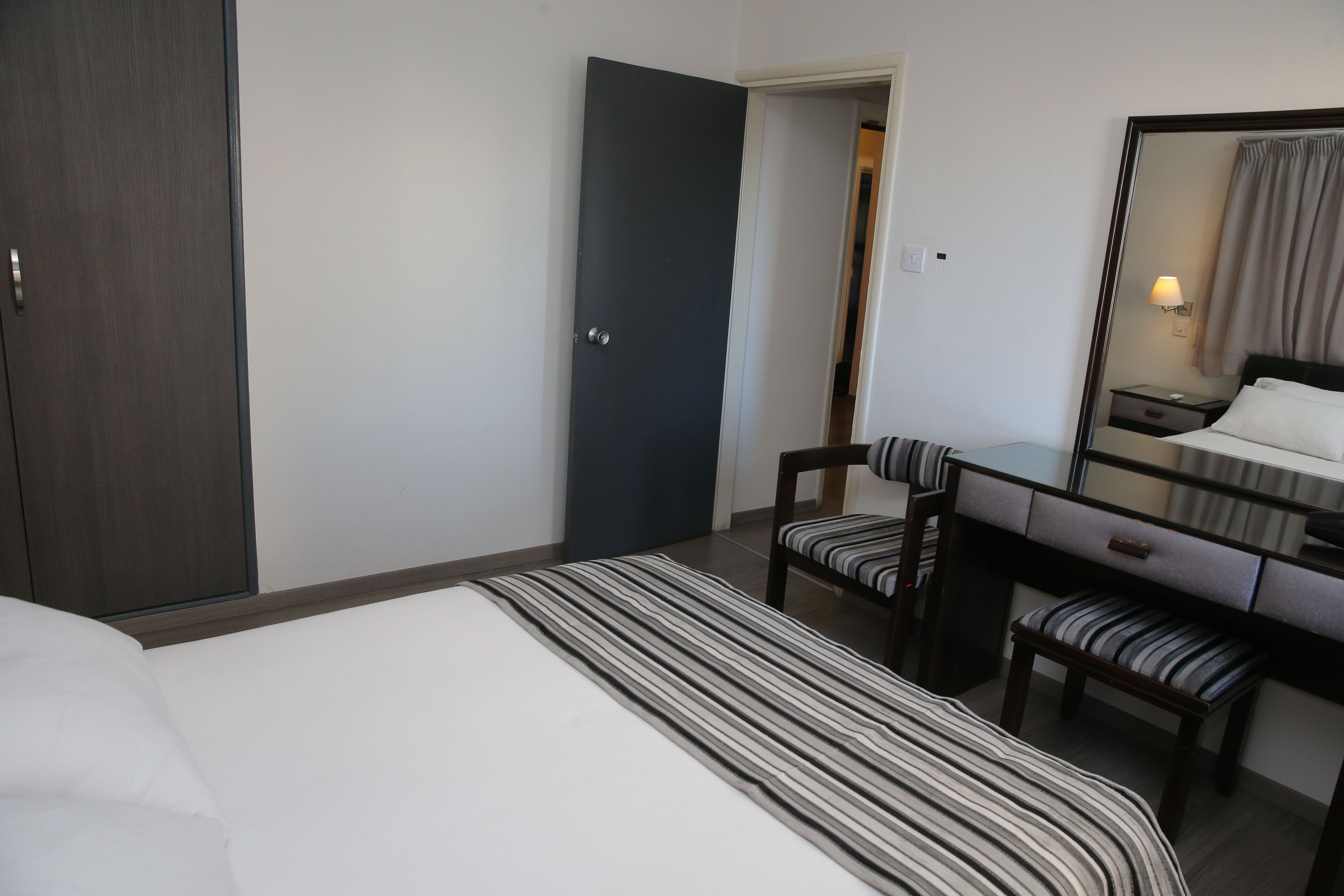 Una habitación de hotel con cama, escritorio, silla, espejo y armario.