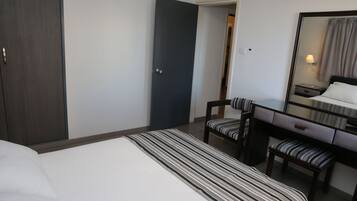 Una habitación de hotel con cama, escritorio, silla, espejo y armario.