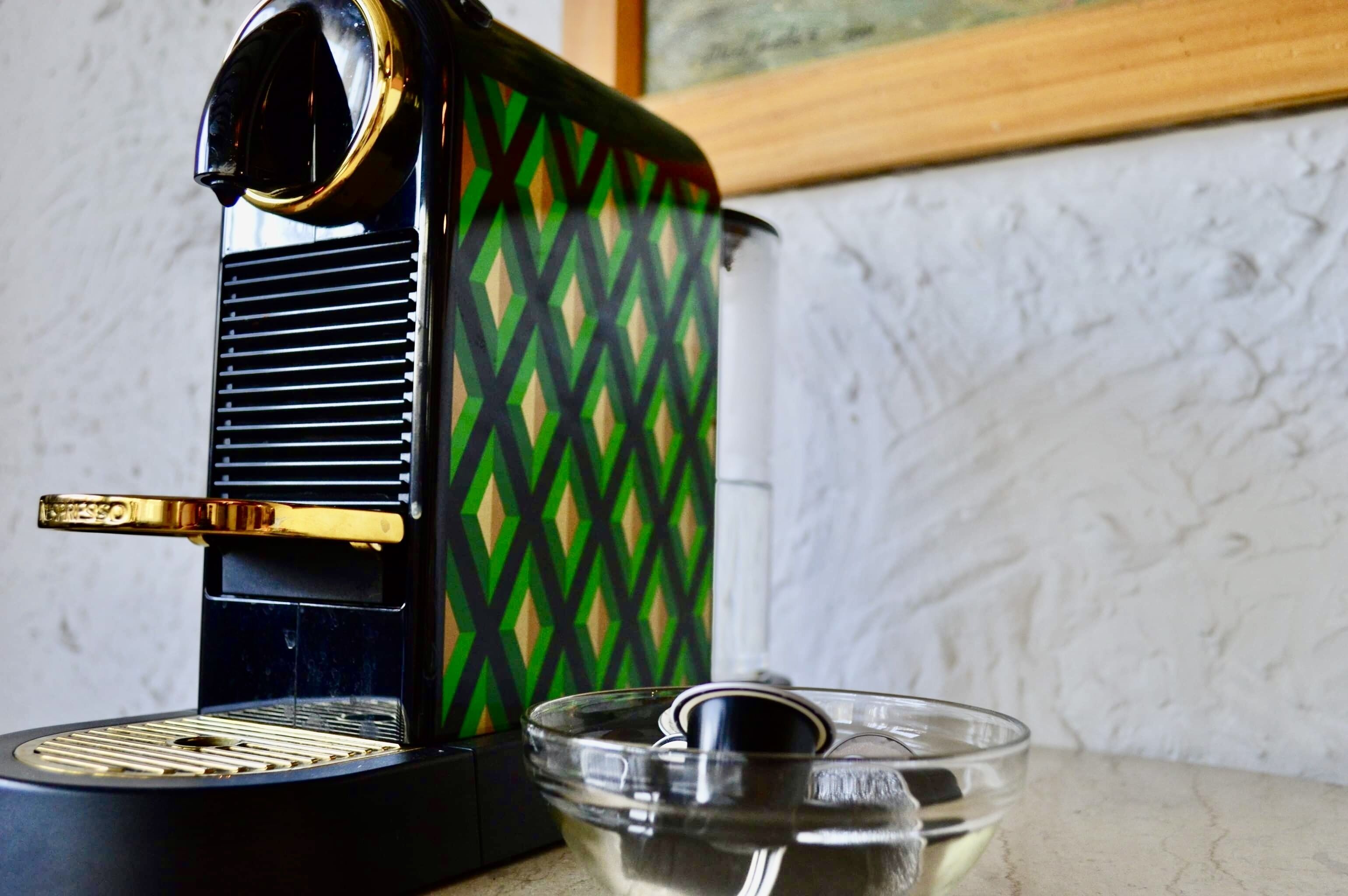 A coffee maker with a green and black diamond pattern, a clear glass carafe, and a metal spoon.