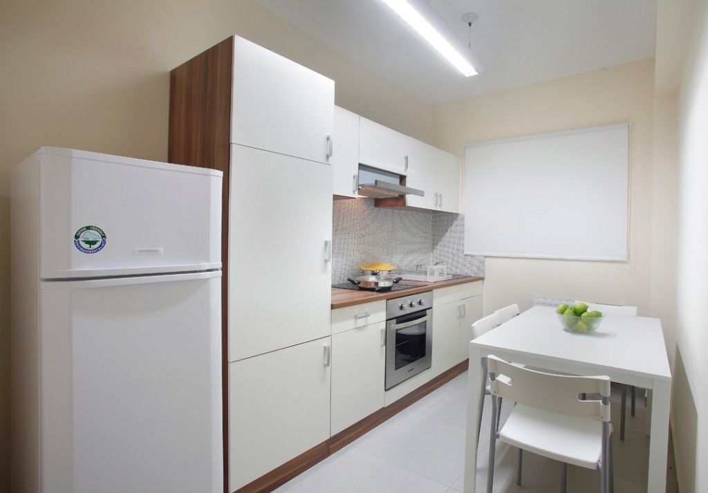 A compact kitchen with white cabinets, a built-in oven, and a white dining table with chairs.