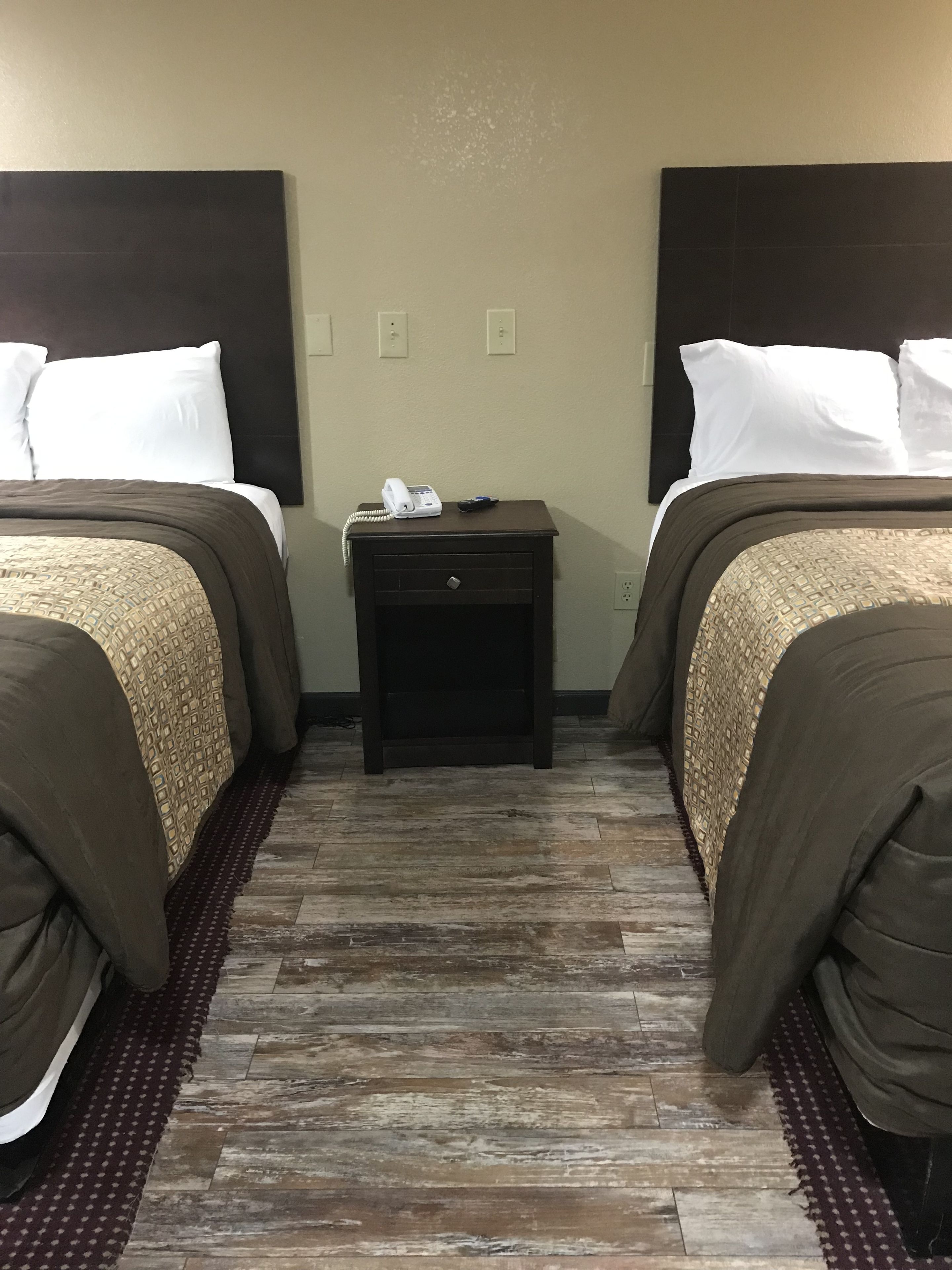 A hotel room with two beds, a small nightstand with a phone, and a wooden floor.