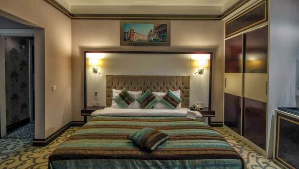 A hotel room with a large bed, a headboard with lights, a painting above the bed, and a wardrobe with sliding doors. - For You Medikent Otel (Atakum)