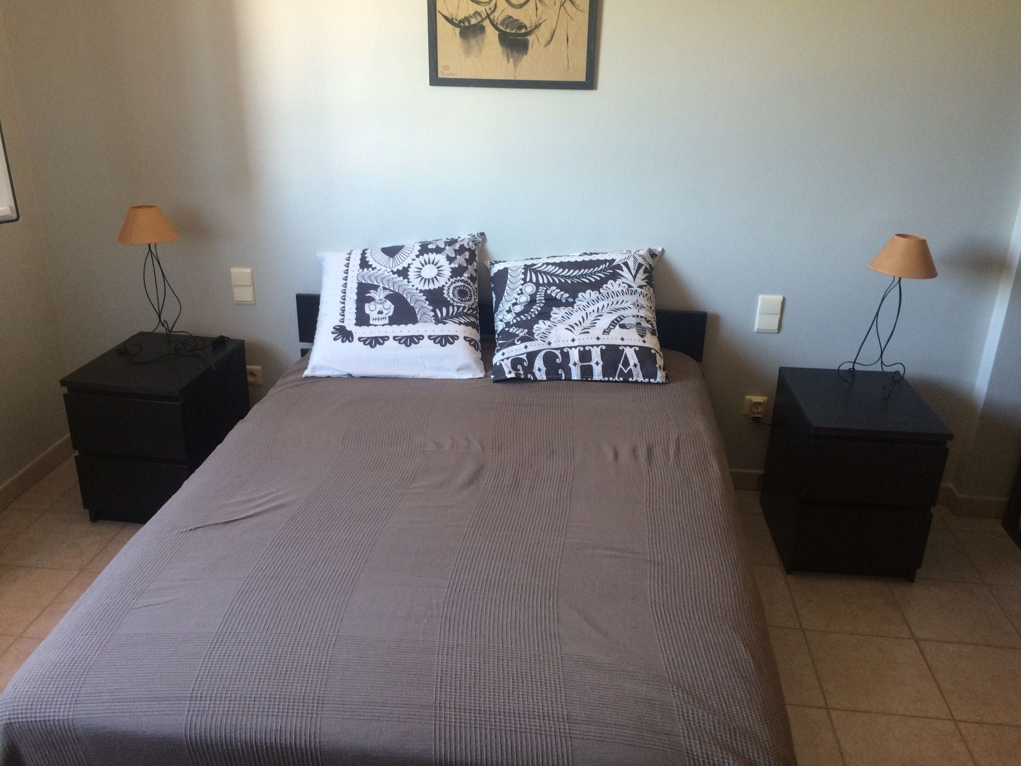 Un dormitorio con una cama grande, dos mesitas de noche, dos lámparas y un cuadro colgado en la pared.