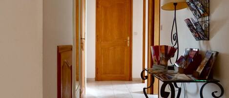 A hallway with a wooden door at the end, a glass table with a lamp, and framed pictures on the walls.