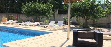 A poolside area with lounge chairs, a glass table, and a pergola.