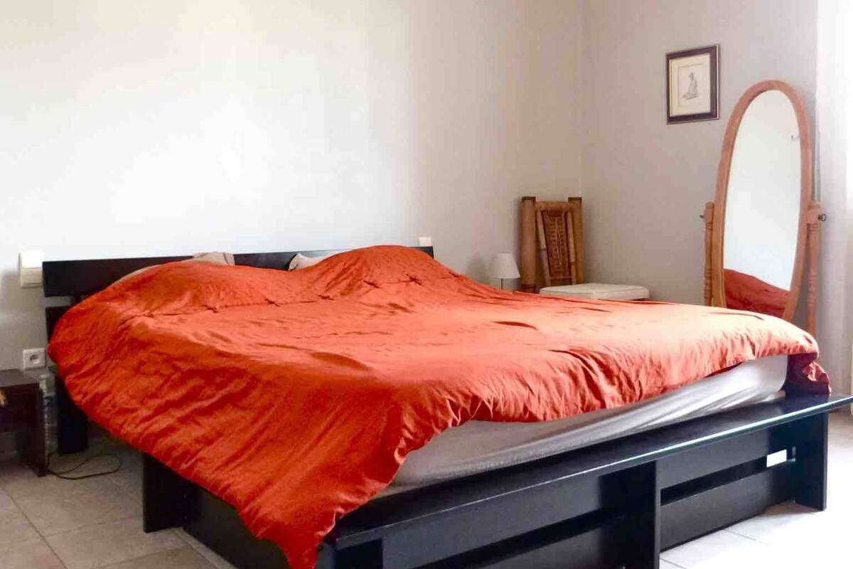 A bedroom with a bed, a bedside table, a mirror, and a wall-mounted picture.