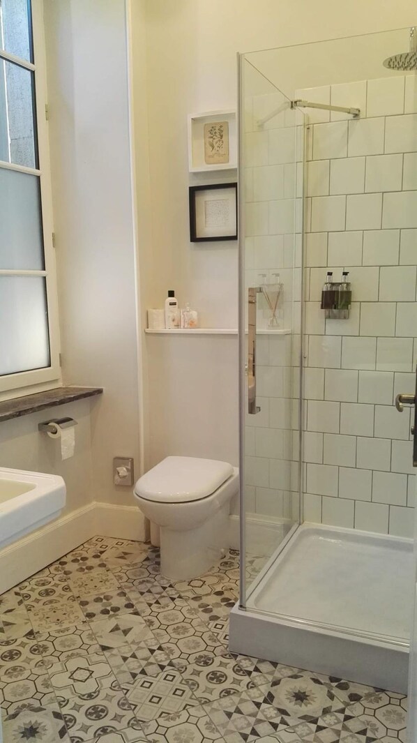 A bathroom with a toilet, sink, shower, and patterned floor tiles. - Maison De L'Aguze (Saint-Pons-de-Thomieres)
