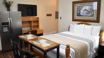 Habitación de hotel con cama, escritorio con computadora, refrigerador, televisor y un cuadro en la pared.