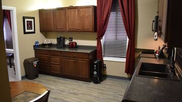 A compact kitchen with wooden cabinets, a coffee maker, and a trash can.