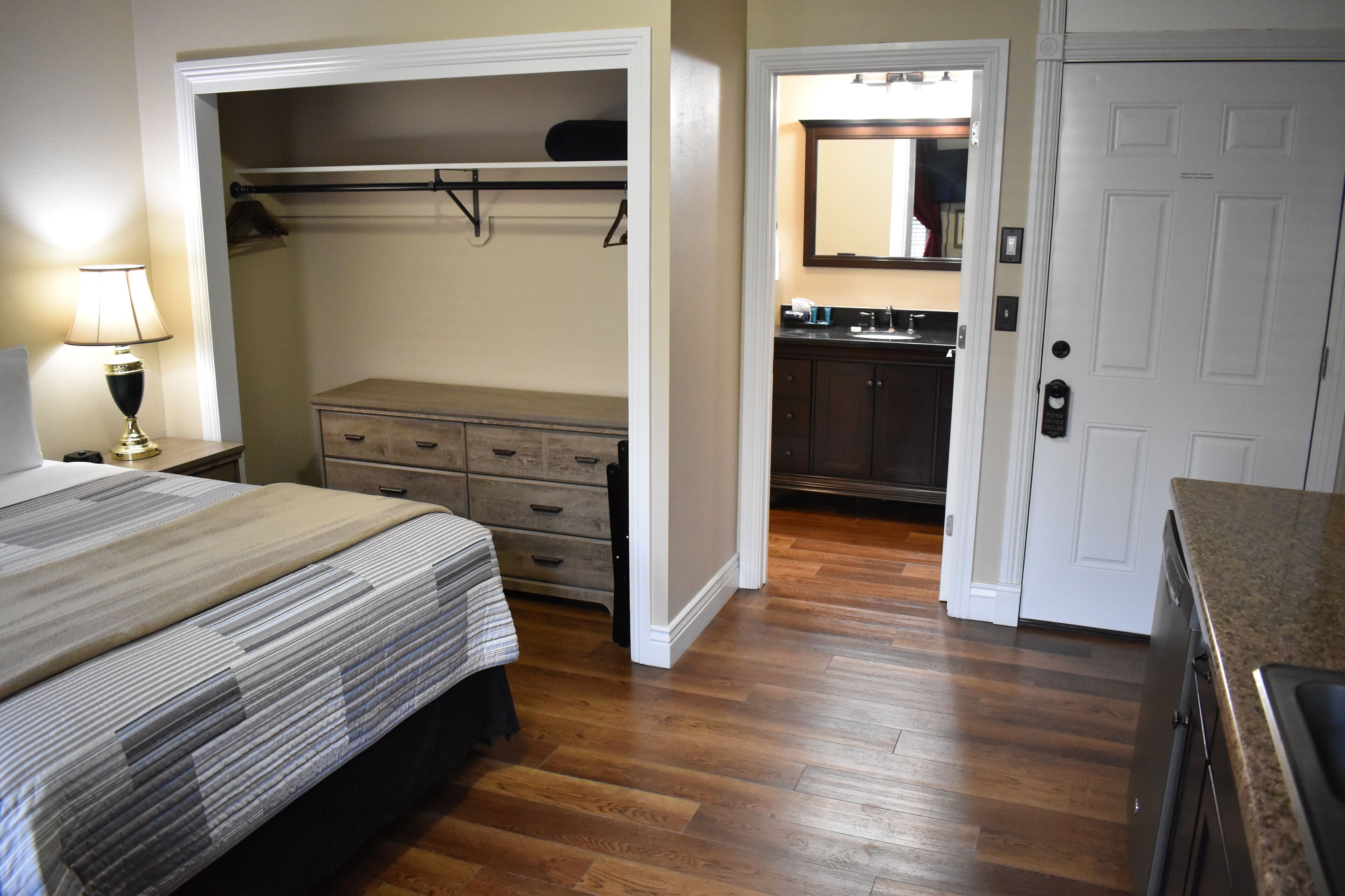 A bedroom with a bed, dresser, and closet. There is a bathroom with a sink and mirror.