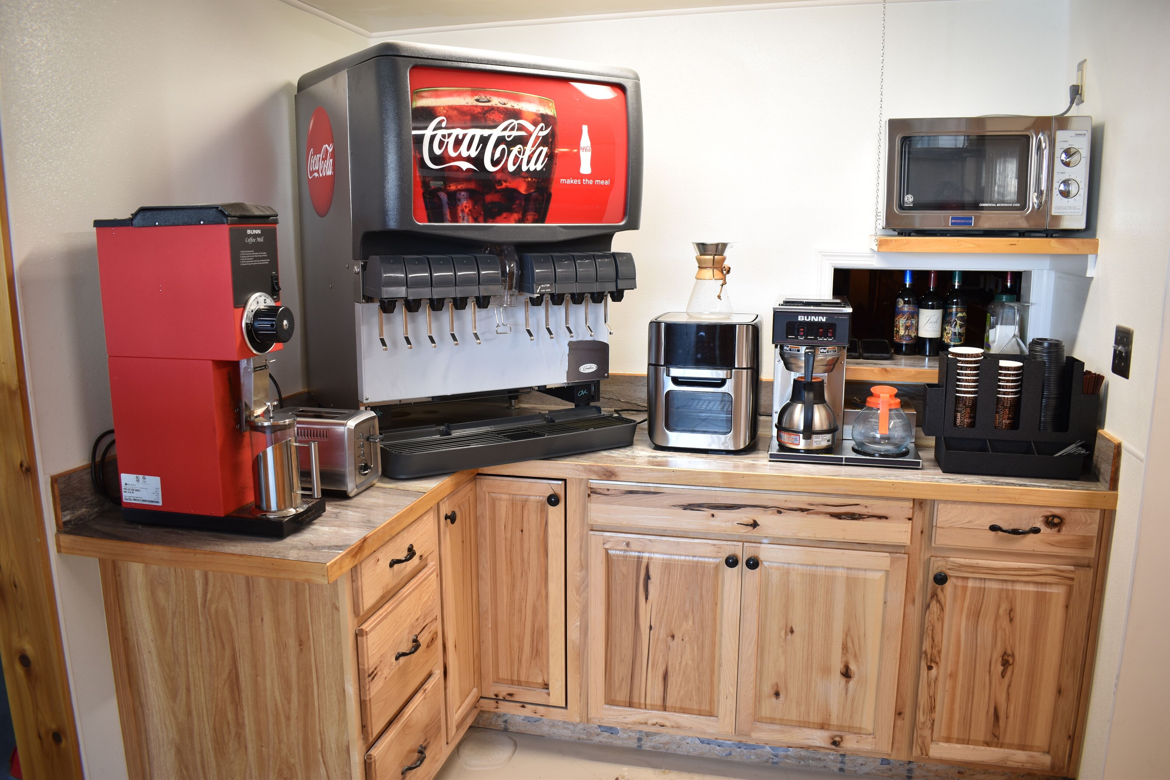 A kitchen with a coffee machine, a microwave, a Coca-Cola dispenser, and a coffee maker.
