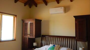 A bedroom with a wooden ceiling, a bed with white linens, two rolled towels, a nightstand with a lamp, and a window with blinds.