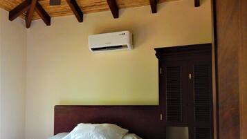 A hotel room with a bed, a ceiling fan, an air conditioning unit, and a wooden wardrobe.