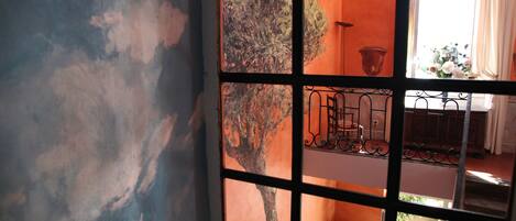 A room with a large window divided into multiple panes, a balcony with a wrought iron railing, and a view of the outdoors.