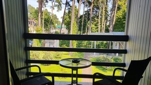 A balcony with two chairs and a small table, overlooking a green lawn and trees. - Valensija M (Jurmala)