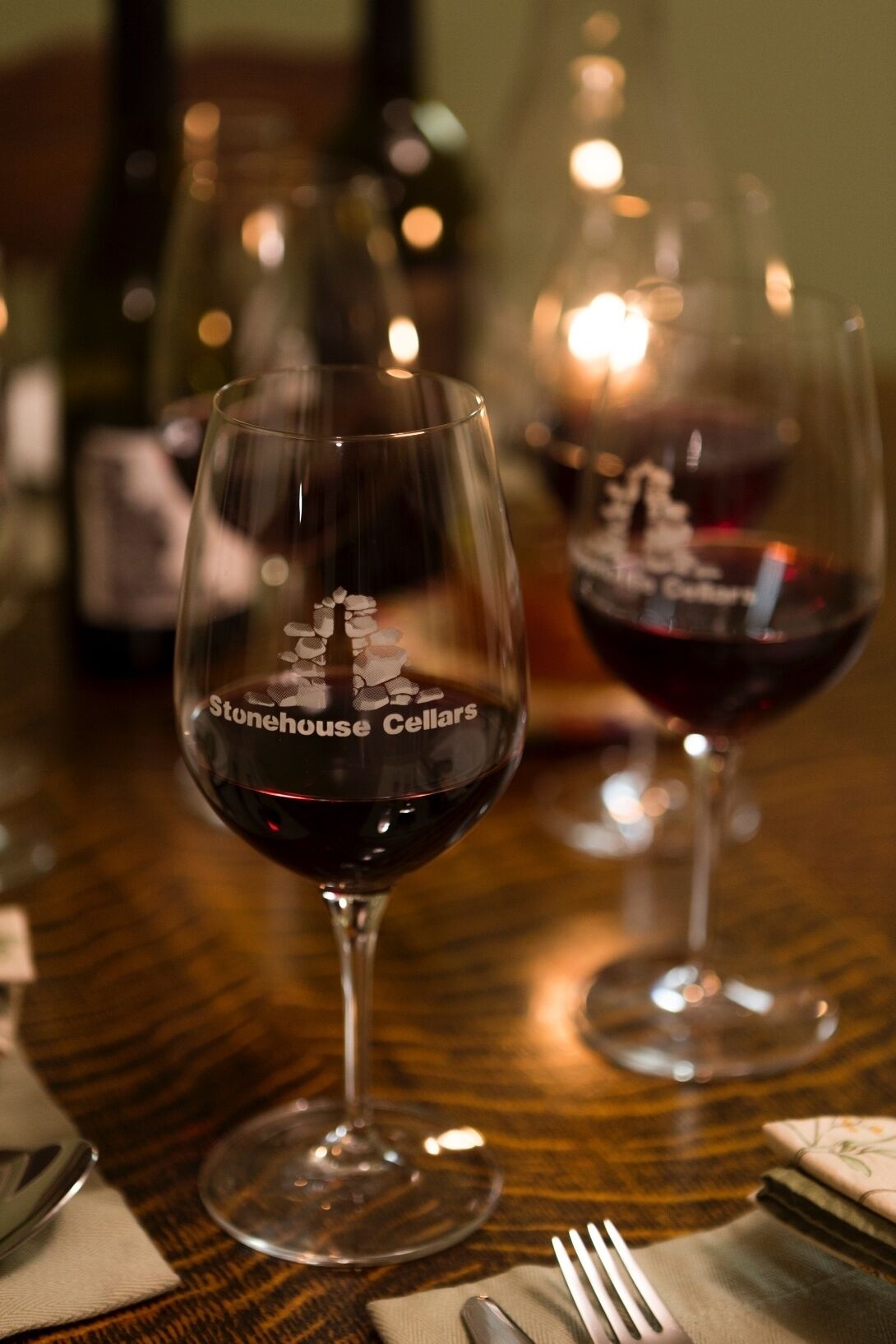 Kaksi viinilasia, joissa on "Stonehouse Cellars" -merkintä, puupöydällä.