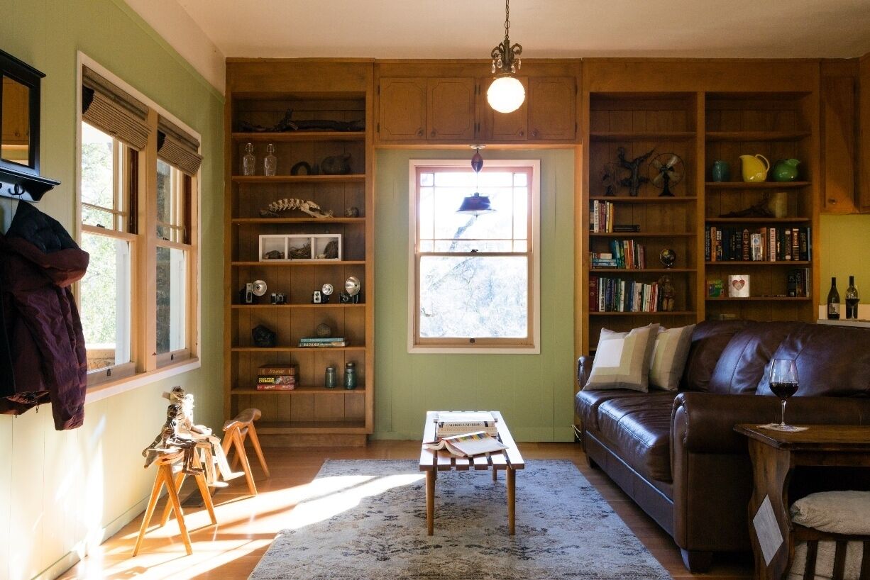 A cozy living room with a leather sofa, wooden shelves, and a large window.